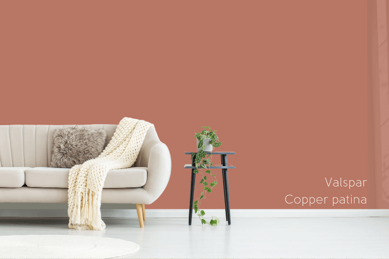 Valspar's Copper Patina Terracotta color on the wall in a living room behind a cream sofa and a plant on a stool, with a white floor.
