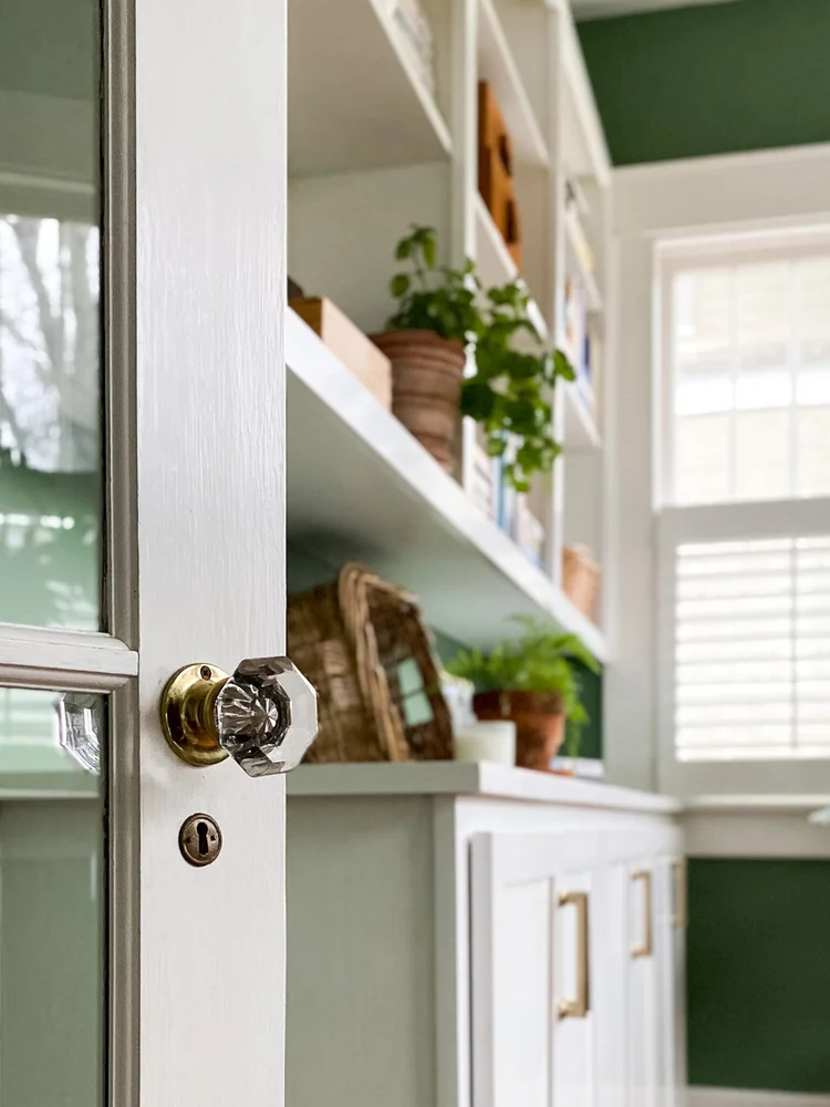 Benjamin Moore Palace green on a back wall in a home office with cabinets and a white glass door in the foreground.