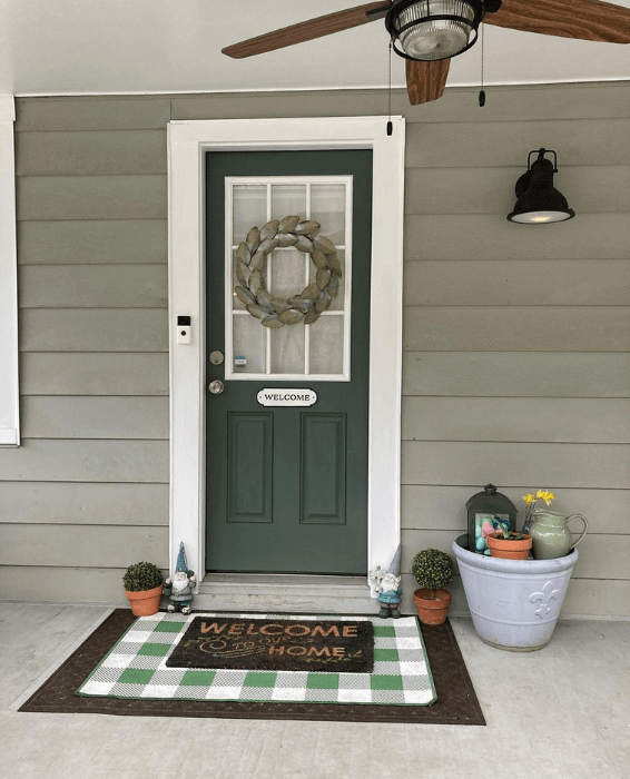 Pewter Green front door says "welcome" with a wreath above on a lighter sage green exterior.