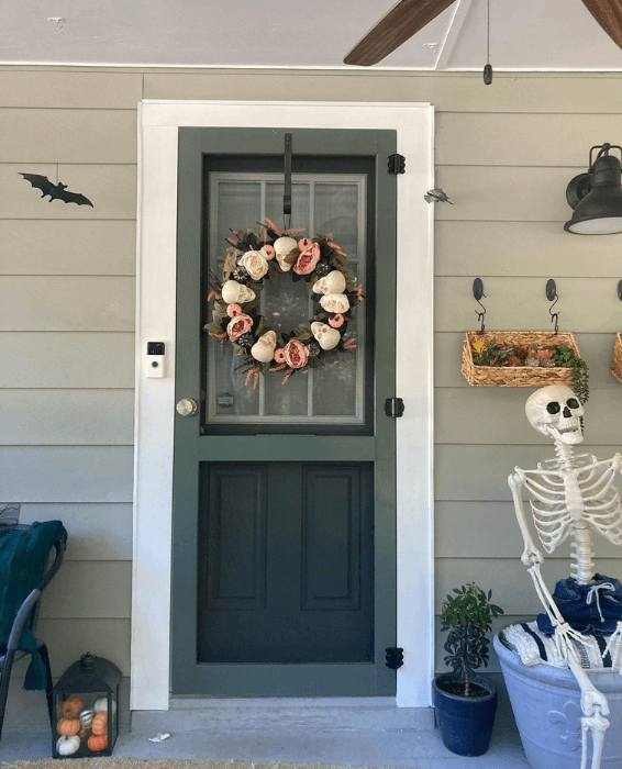 Pewter Green front door with matching screen door, decorated for halloween on a lighter sage green exterior. A skeleton sits to the right of the door.