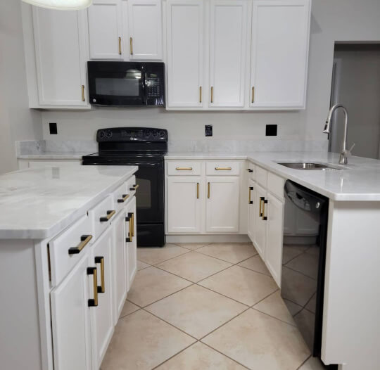 White Snowbound cabinets in a kitchen with black appliances and beige tile