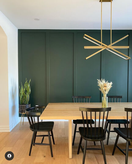 Essex Green on a wall behind a natural wood table with black chairs and a brass chandelier