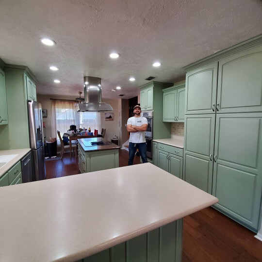The owner of GR Cabinet Painting poses in a kitchen that was transformed from golden oak to SW Clary Sage