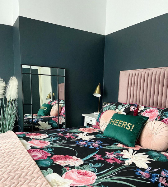 A dark blue green bedroom with white on the upper 1/4. Bed has similar colors with pink accents.