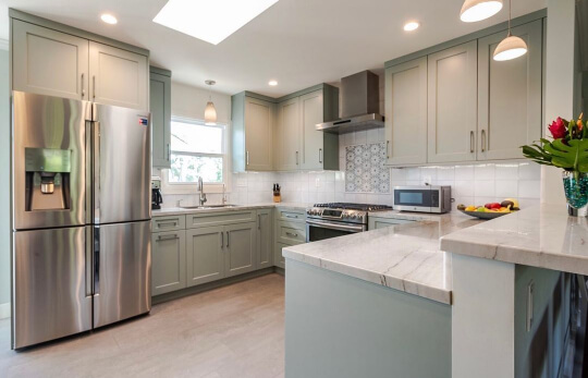 Misted Green cabinets with pewter hardware with white tile and light stone countertops