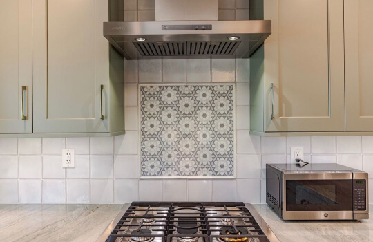 Misted Green cabinets with pewter hardware with patterned tile behind stove  and light stone countertops