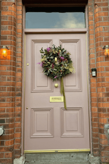 Sulking room pink on a front door of a brick house with a wreath