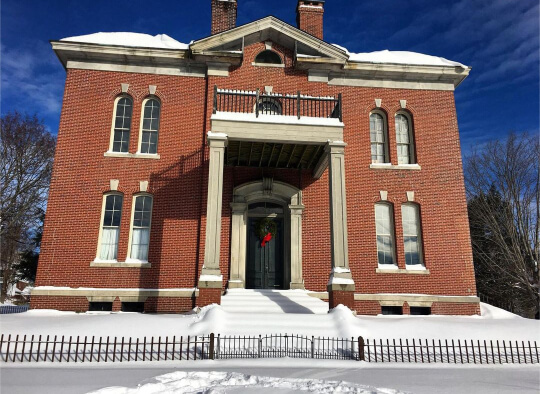 An imposing brick home that used to be a government building, on a snowy day.