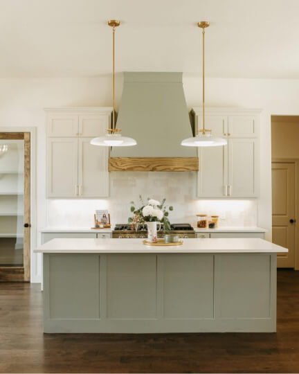 Sherwin Williams Evergreen Fog on a custom hood fan and island in a kitchen with Gossamer veil wall cabinets, white stone countertops, and glass pendant lights.