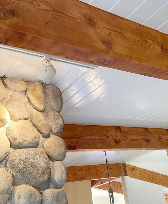 Semi gloss simply white shiplap panels on a ceiling with warm wood beams and a natural river rock fireplace
