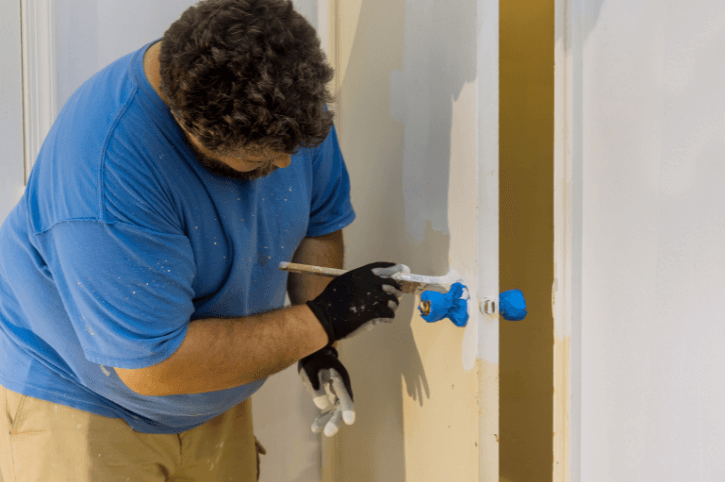 Man paints around taped off door hardware
