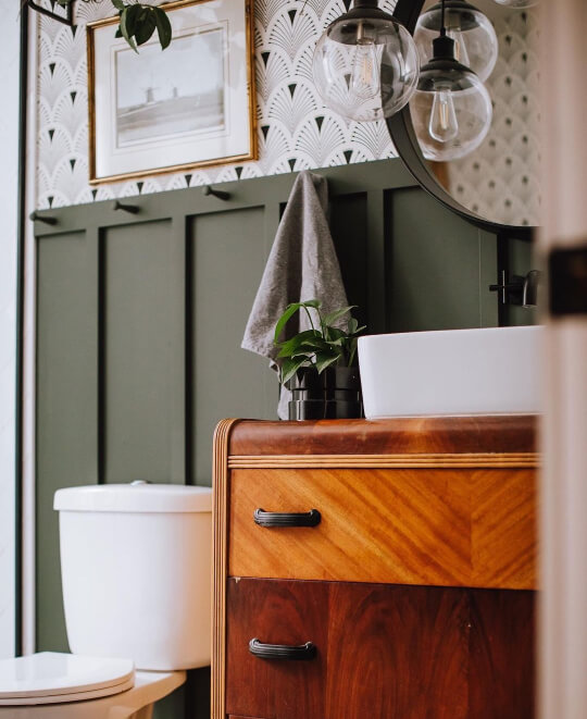 Benjamin Moore Pewter Green lookalike Vintage Vogue on Board and Batten wall behind a vintage wood vanity in a bathroom with a white sink and black built-in faucet