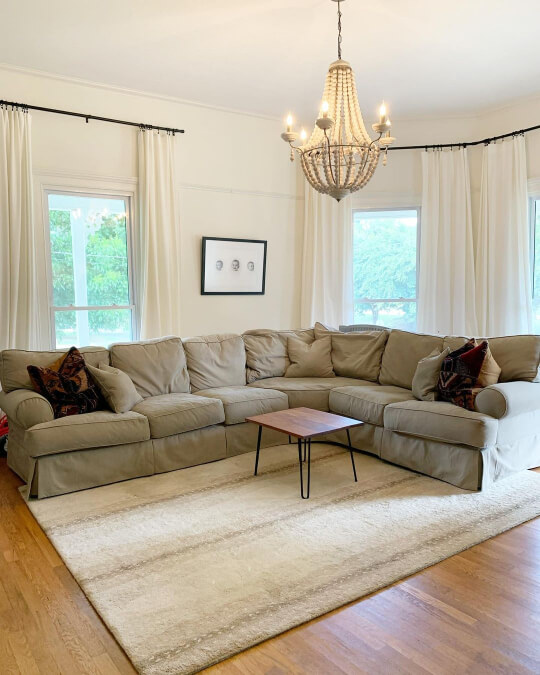 Alabaster Living room walls and trim with an oversized sectional, white area rug, a chandelier, and big windows with matching creamy white drapes.