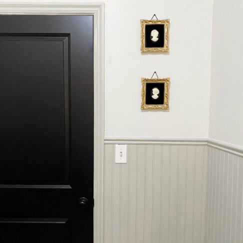 A tricorn black interior door with a soft greige green trim and wainscoting and creamy white walls.