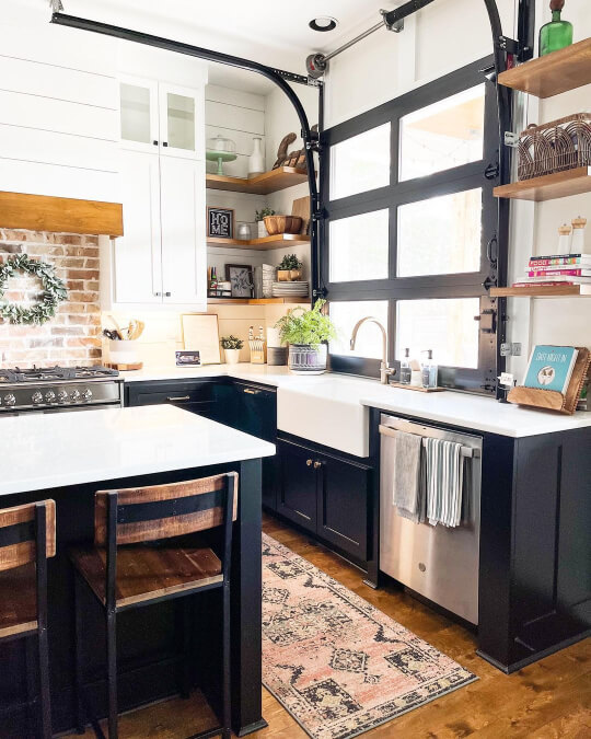 White upper cabinets with black lower cabinets and island, wood floors, and a funky garage door in the wall