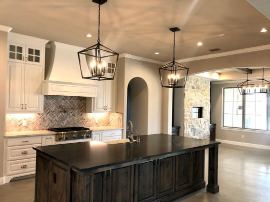 Large stained black island with creamy white perimeter cabinets, beige walls, and geometric pendant lights