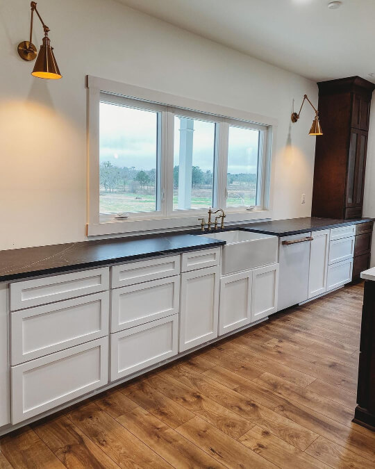Long white run of Greek Villa lower cabinets with no upper cabinets in a two toned kitchen with dark wood pantry in corner