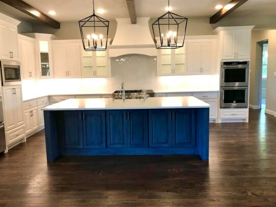 White cabinets against a wall in a large kitchen with custom white hood vent and navy blue island with white countertops