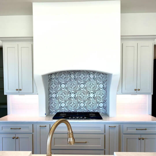 Oversized plaster hood vent in bright white with a silvery gray blue paint on cabinets and portuguese inspired tile behind the stovetop