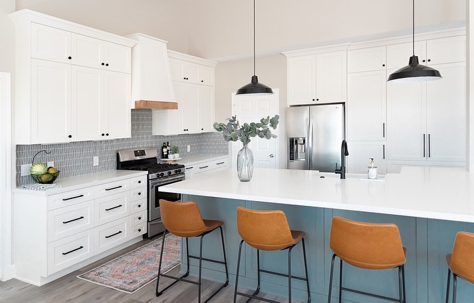 Two Tone kitchen with white cabinets all around the room and a teal island. 4 mustard leather bar stools sit at the island with black pendant lamps overhead