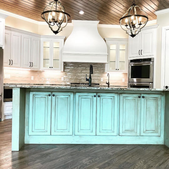 White cabinets with seafoam green antiqued island and bright overhead lighting in dark wood ceiling