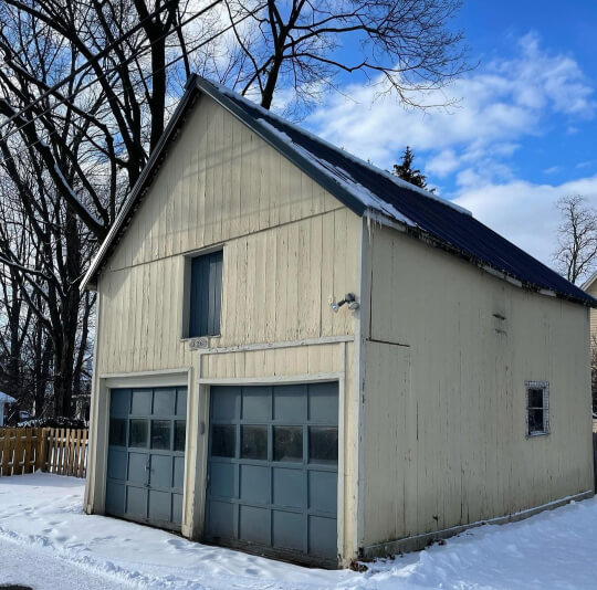 Garage exterior before Cascades, butter yellow barn style with dark green garage doors and trim