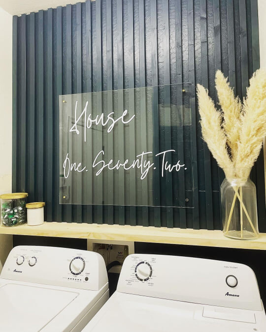 Cascades on laundry room feature wall with a sign that reads house one seventy two