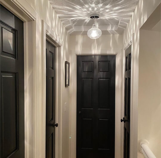 Dove Wing in the scattered light of a chandelier in a hallway with all black doors and Valspar Snowed In trim