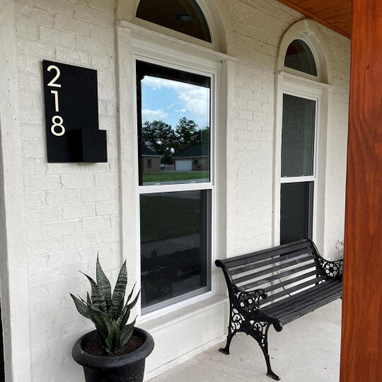 Sherwin Williams Oyster White Painted Brick front porch area of a house with cedar beams and white windows. House number reads 218 on a black sign.