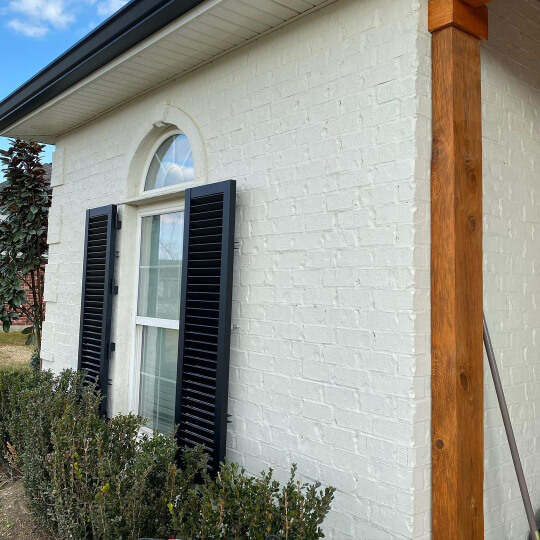 Sherwin Williams Oyster White Painted Brick exterior of a house with Tricorn Black shutters, cedar beams, and white window trim 
