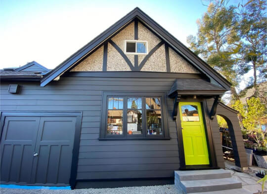 Wide angle shot of a small tudor home with exterior siding painted in Iron Ore with black trim and lime front door