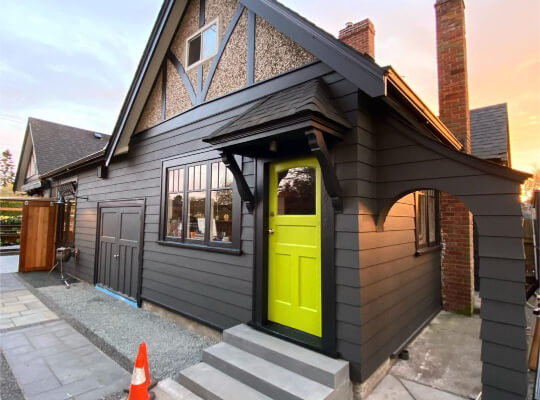 Iron Ore siding with black trim and a lime door on a small tudor house in front of the sunset