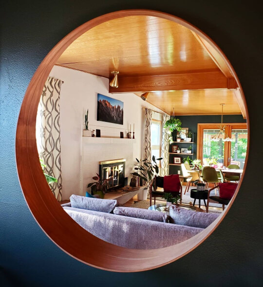 A round wood mirror on a Rock Bottom living room wall, with the rest of the room and opposite rock bottom wall reflected inside.