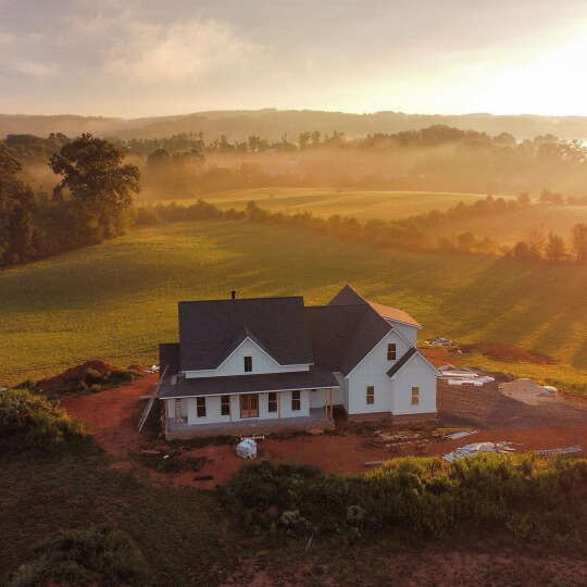 An epic drone shot of Alabaster siding on a white farmhouse at sunrise in front of rolling hills.