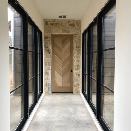 Alabaster in a long hallwy with a wood door at the end and black framed breezeway windows