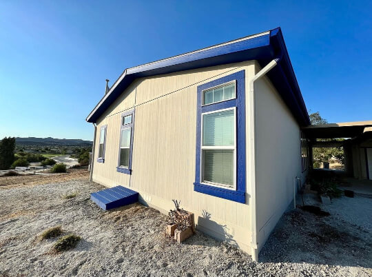 Front side angle of Accessible Beige exterior with Royal Blue trim on a small home on a sunny day with a bright blue sky