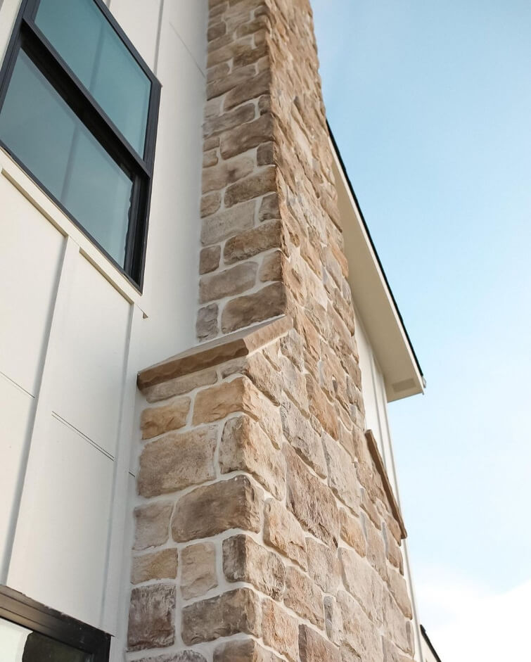 A close up of creamy white dove at sunset on a two storey exterior with an organic brick chimney running up the side