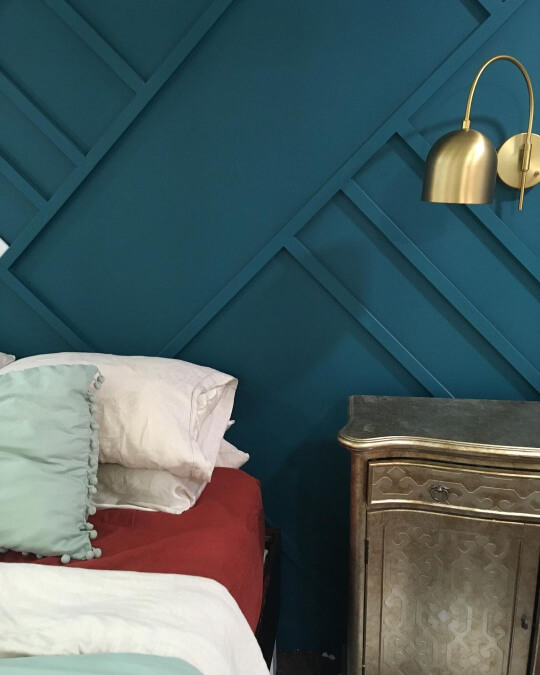 Closeup of Sherwin Williams Blue Peacock on a feature wall in a bedroom with a brass wall sconce light fixture