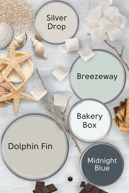 Behr Dolphin Fin in a cool beachy color palette featuring Breezeway, Bakery Box, Silver Drop, and Midnight Blue, with Dolphin Fin, all on paint lids over a beachy backdrop of gray with sea shells, marshmallows and sticks, and s'mores supplies