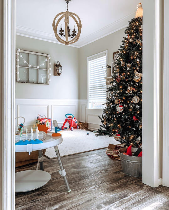Behr Silver Drop on a living room wall with white wainscoting on the lower half. Toys are scattered on the floor over a white rug, baby's skip hop and a Christmas tree display.