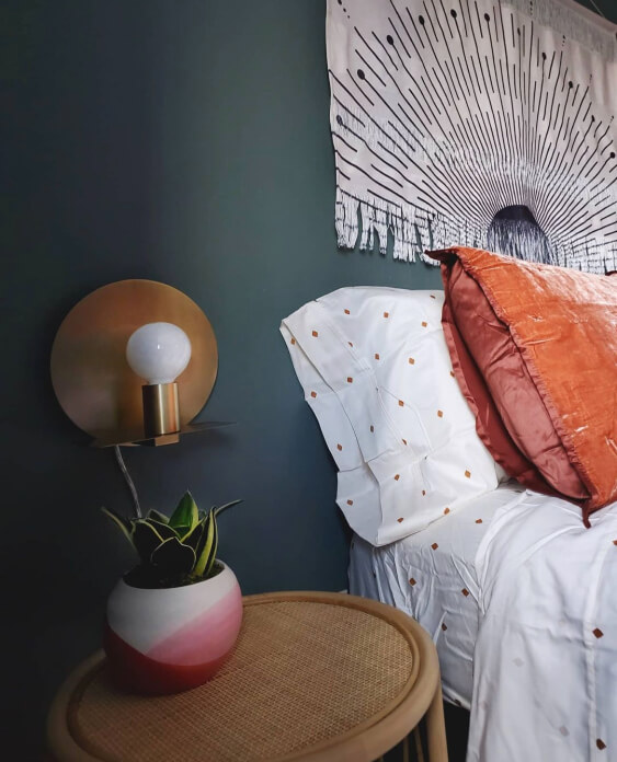 Sherwin Williams Succulent on the walls behind a bed with white polka dotted sheets and a little side table with a copper lamp and a potted succulent.