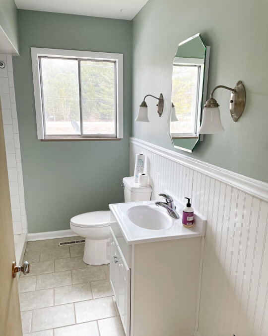 Sherwin Williams Comfort Gray on walls in a bathroom with white beadboard on the lower half of the vanity wall. Two wall sconces frame the simple mirror.