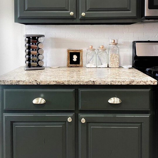 Sherwin Williams Shade Grown dark sage cabinets with silver hardware and beige stone countertops