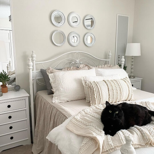 Classic Gray on bedroom walls behind an arrangement of small circle mirrors above a bed with neutral linens