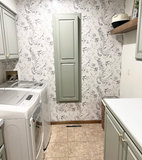 Oyster Bay on cabinets and built-in iron board. Washing machine and dryer with plants and birds wallpaper.