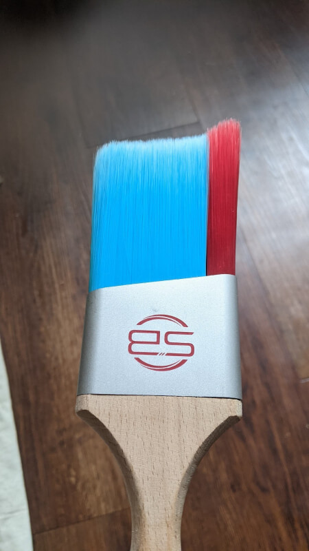 Closeup photo of a brand new version of the 2.5" Stinger Brush. A blue and red paint brush with the SB logo and a wooden handle