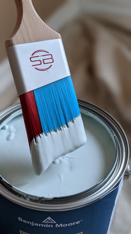 Blue and red Stinger Brush dipped in minty colored paint and held over a paint can