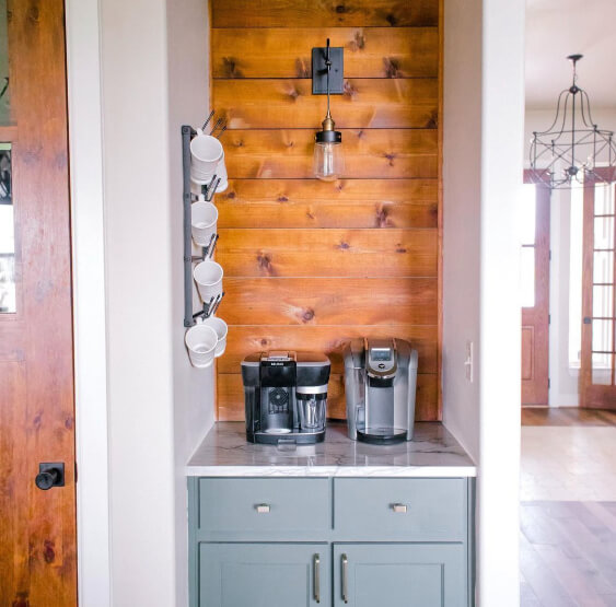 Pewter Green looking like a blue sage color on kitchen cabinets in a small coffee bar corner with white marble countertops and a wood wall