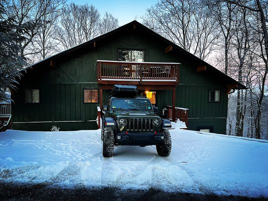 A 4 wheel drive vehicle in the snowy driveway of a home painted in Sherwin Williams Ripe Olive