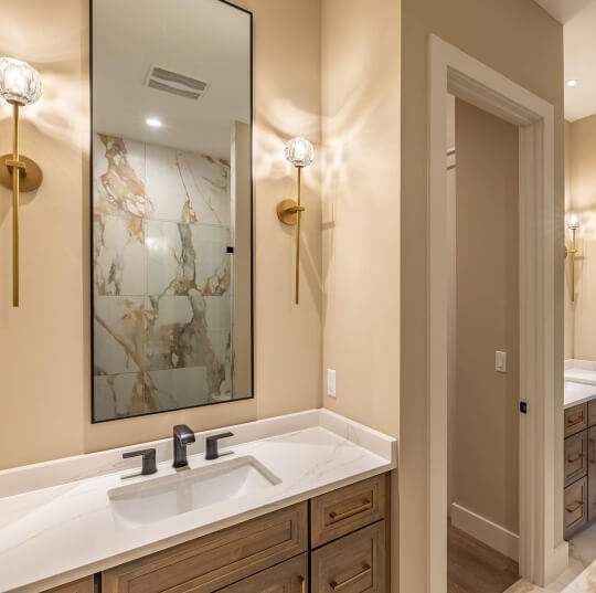 Sherwin Williams Shiitake on the walls in a bathroom with a tall rectangle mirror hanging above an oak vanity with two sconce lights on either side of the mirror.